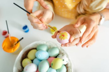 top view of kid painting easter egg near mother on white 