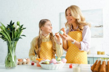 selective focus of happy daughter and mother near easter eggs and flowers