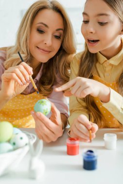 selective focus of happy kid pointing with finger at painted easter egg near mother 