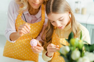 selective focus of cute child near mother painting easter egg and tulips 