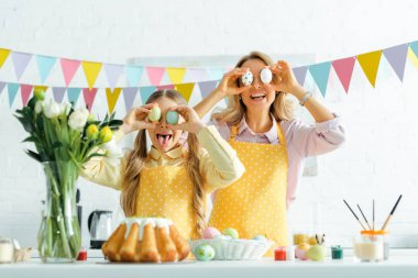 cheerful daughter and mother covering eyes with painted easter eggs 