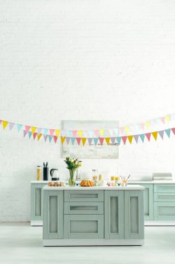modern kitchen with baked easter cake, painted chicken eggs and flowers in vase