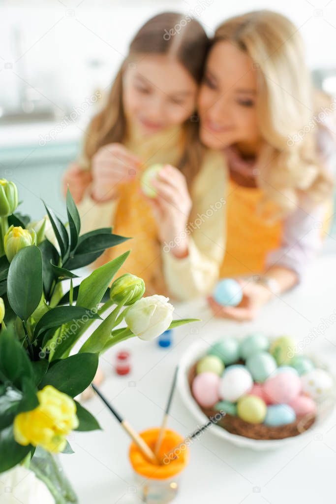 selective focus of tulips near mother and daughter painting easter eggs
