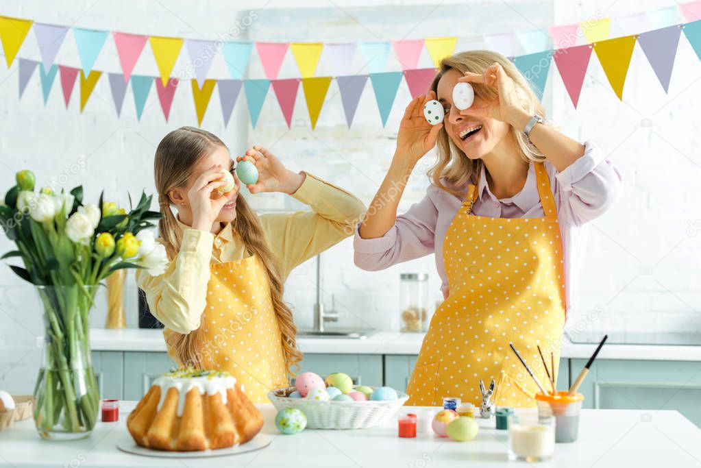 happy daughter and mother covering eyes with painted easter eggs