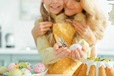 cropped view of happy mother hugging daughter holding decorative rabbit and painted easter egg 