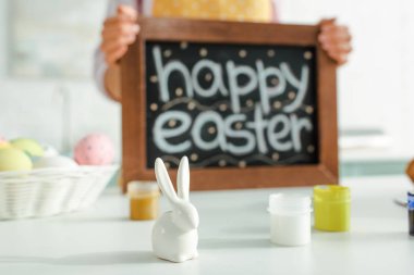selective focus of decorative rabbit near woman holding chalkboard with happy easter lettering 