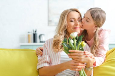 cute daughter kissing happy mother holding bouquet of tulips 