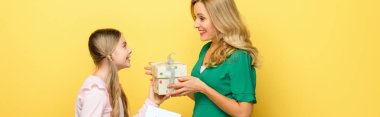 panoramic shot of happy kid giving present to mother isolated on yellow 