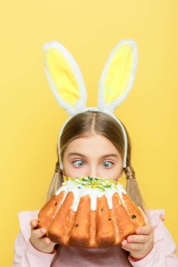 cute kid with bunny ears looking at easter cake isolated on yellow 