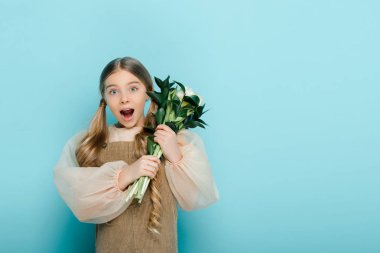 shocked kid holding bouquet of flowers on blue 