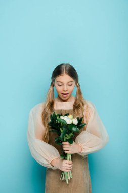 surprised kid holding bouquet of flowers on blue 