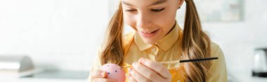 panoramic shot of happy kid painting easter egg with paintbrush 