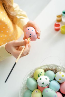 top view of kid painting easter egg with paintbrush at home