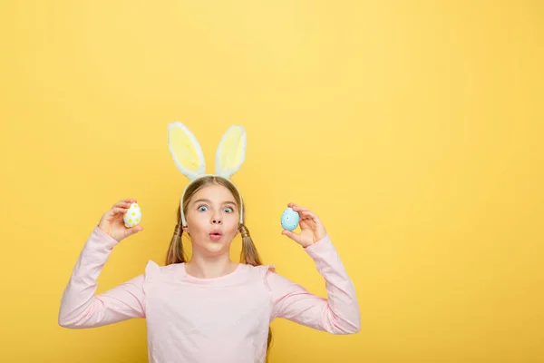 Шокована Дитина Вухами Кролика Тримає Розфарбовані Великодні Яйця Ізольовані Жовтому — стокове фото