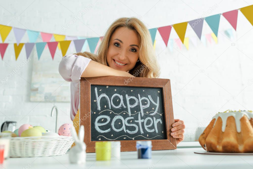 selective focus of cheerful woman holding chalkboard with happy easter lettering 