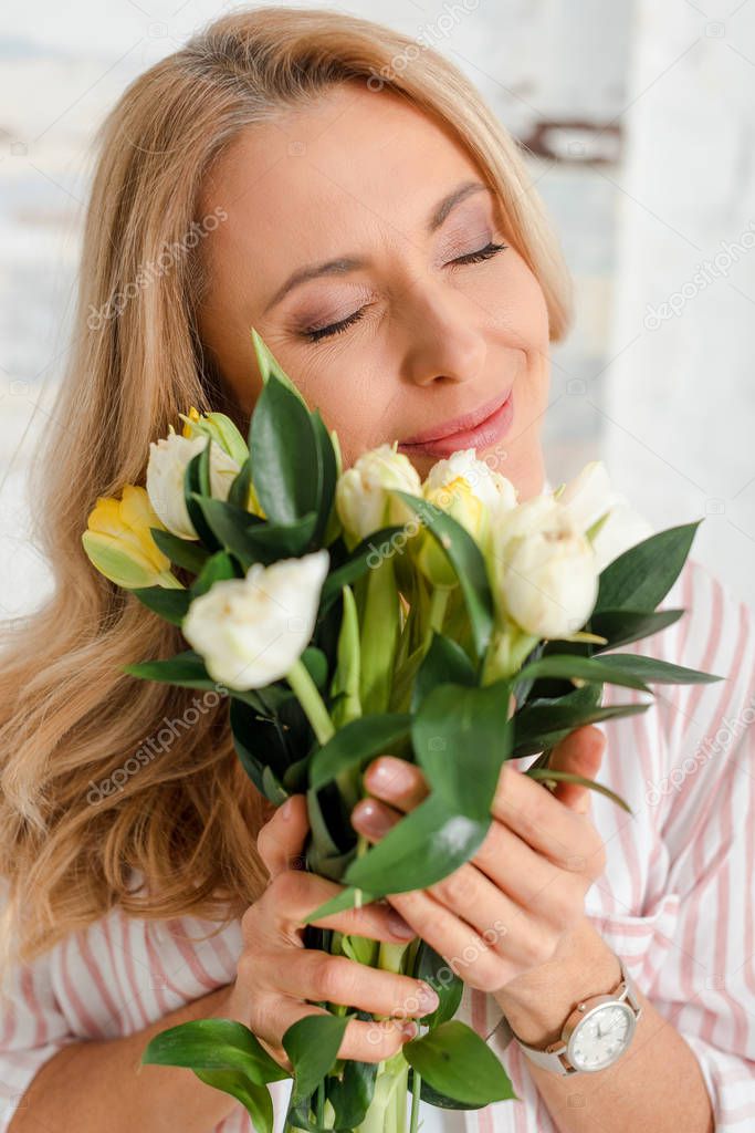 selective focus of happy woman with closed eyes holding bouquet of tulips 