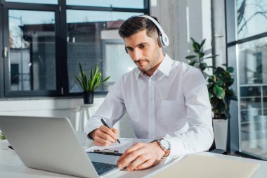 Çevrimiçi çalışan yakışıklı erkek çevirmen kulaklık ve dizüstü bilgisayarla