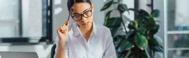 panoramic shot of thoughtful asian translator working in office clipart