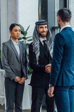 multiethnic smiling business partners shaking hands on meeting with translator in office clipart