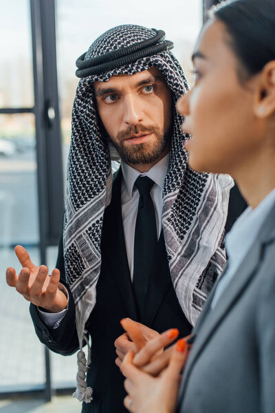 selective focus of arabic businessman talking with businesswoman in modern office 