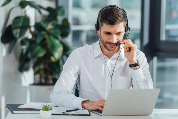 Улыбающийся переводчик-мужчина, работающий онлайн с гарнитурой и ноутбуком
