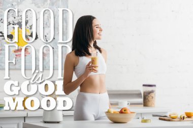Çekici fit sporcu kadın gülümsüyor ve iyi yiyeceklerin yanında bir bardak smoothie tutuyor.