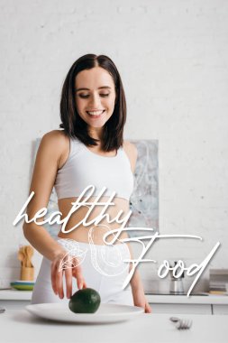 Low angle view of smiling sportswoman taking avocado in kitchen
