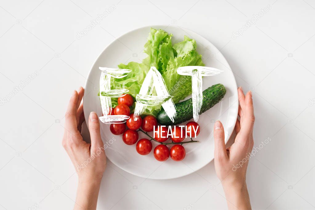 Top view of woman holding plate with raw vegetables on white background
