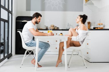 Mutfakta kahvaltıda erkek arkadaşıyla flört eden sütyenli ve gömlekli şehvetli kadının yan görüntüsü.