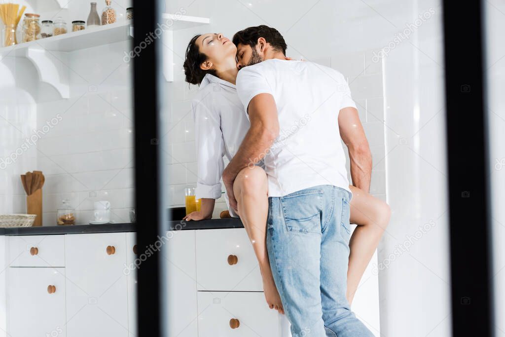Selective focus of handsome man kissing and touching sexy woman on kitchen worktop