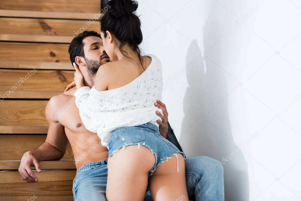 Sexy woman kissing muscular boyfriend on ladder at home 