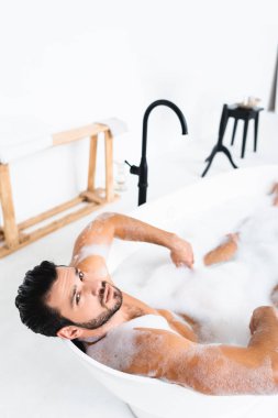 Banyoda banyo yaparken kameraya bakan yakışıklı adamın yüksek açılı görüntüsü.