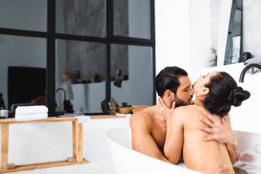 Handsome man kissing and hugging naked girlfriend in bathtub  clipart