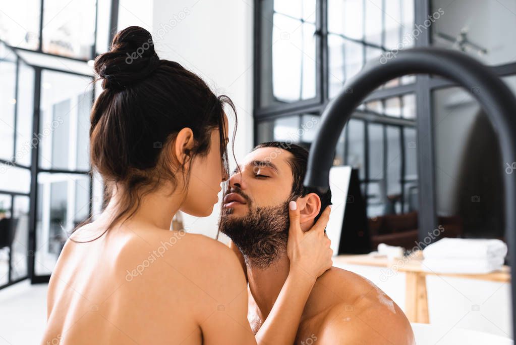 Beautiful naked woman kissing handsome boyfriend in bathtub 