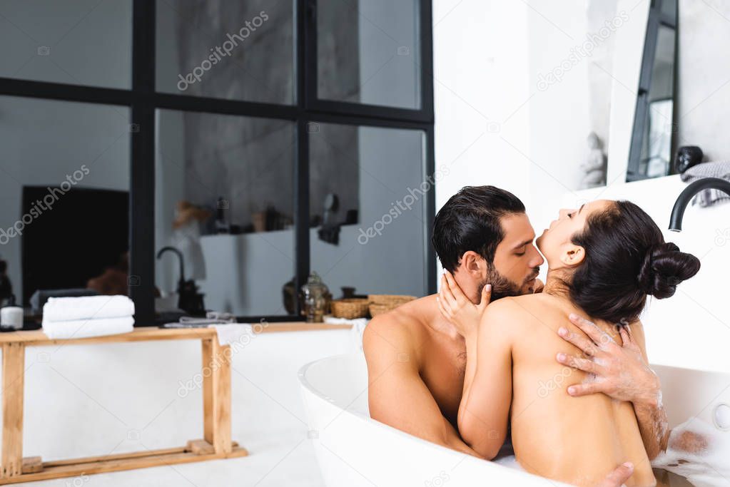 Handsome man kissing and hugging naked girlfriend in bathtub 