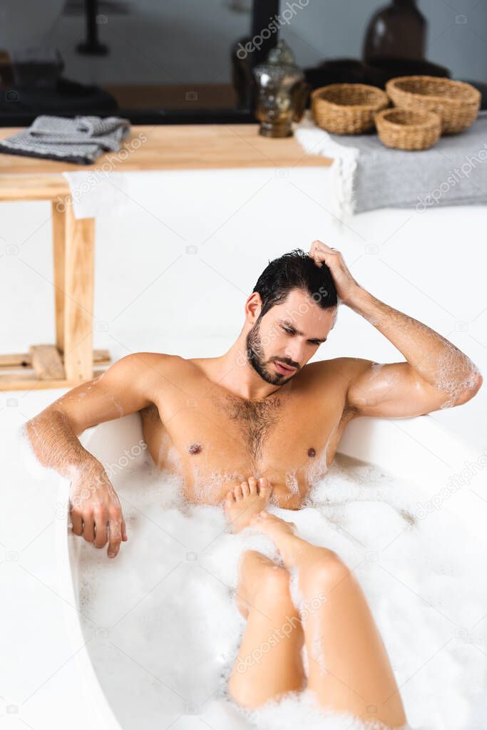 Muscular man looking away while taking bath with girlfriend at home