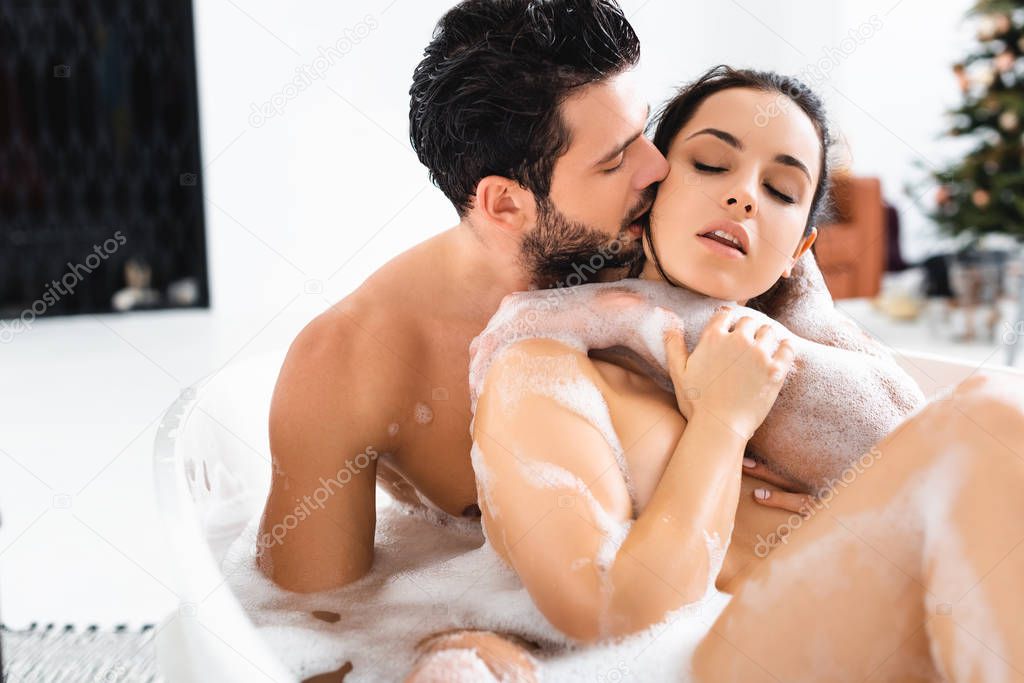 Handsome man kissing and embracing naked girlfriend while taking bath together