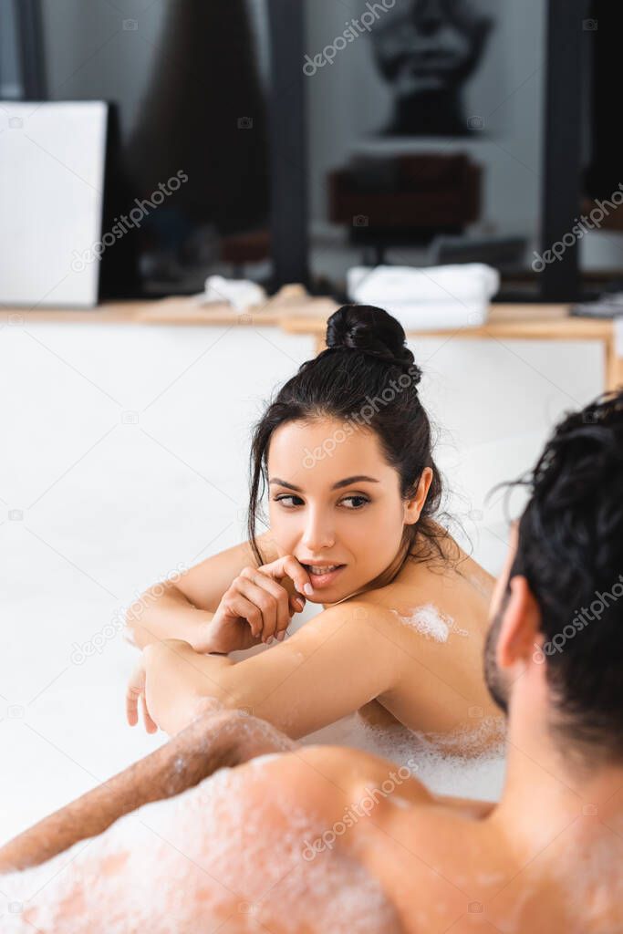 Selective focus of beautiful naked girl flirting with boyfriend in bathtub with soapsuds 