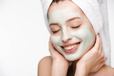 Yüzünde maske ve havluyla gülümseyen bir kız. Yüzüne dokunuyor, gözleri kapalı, beyaz tenli.