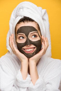 Yüzünde kilden maske ve kafasında havlu olan neşeli bir kız. Yüzüne yakın el ele tutuşup sarıya bakıyor.
