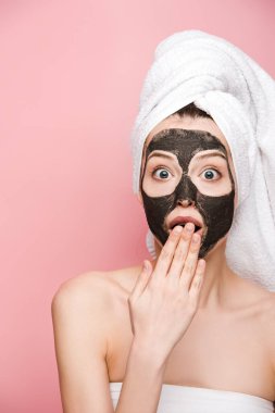 Yüzünde kilden bir maske, ağzında bir elle pembe bir kameraya bakan şok olmuş bir kız.