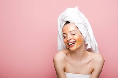 cheerful girl with facial mask and towel on head smiling with closed eyes isolated on pink clipart