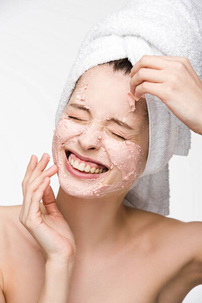 smiling girl with closed eyes removing peeling mask from face isolated on white