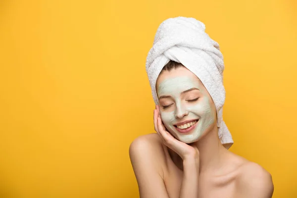 happy girl with nourishing facial mask touching face with closed eyes isolated on yellow