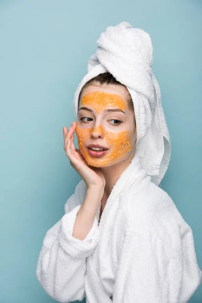 pensive girl with citrus facial mask touching face isolated on blue