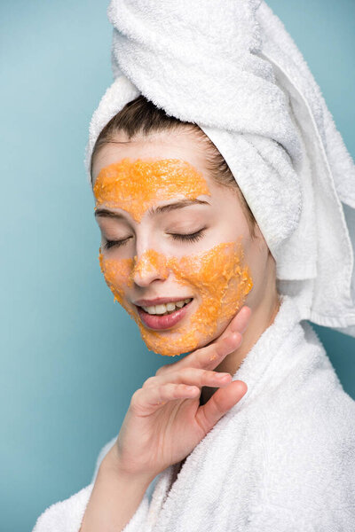 улыбающаяся девушка в цитрусовой маске, касающаяся лица с закрытыми глазами на синем фоне
