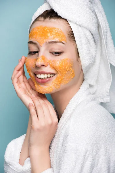 cheerful girl with citrus facial mask touching face isolated on blue