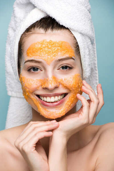 счастливая девушка в цитрусовых маске для лица, держась за руки возле лица и глядя в камеру
