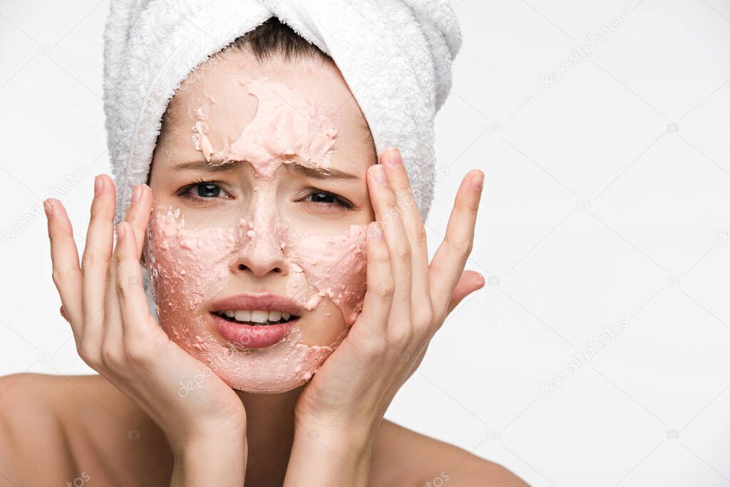 displeased girl with peeling facial mask touching face and looking at camera isolated on white