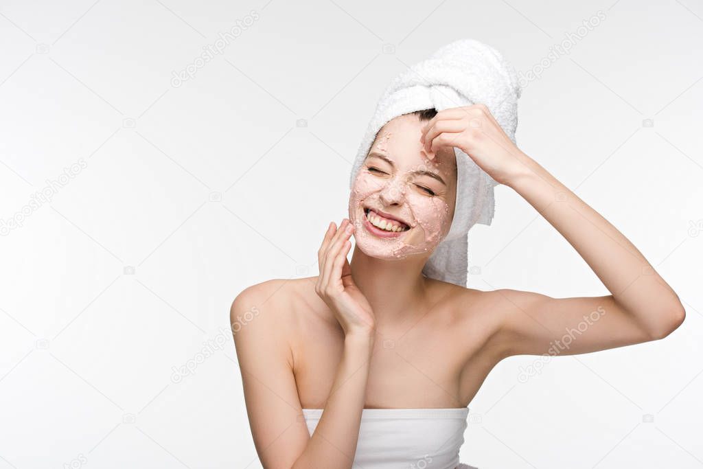 cheerful girl with closed eyes removing peeling mask from face isolated on white